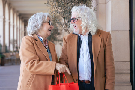 Happy Caucasian senior couple shopping with bags in an elegant urban settingの写真素材