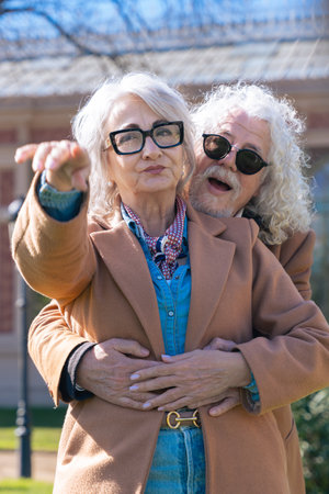 Caucasian senior couple hugging and pointing at something outdoors in sunny parkの写真素材