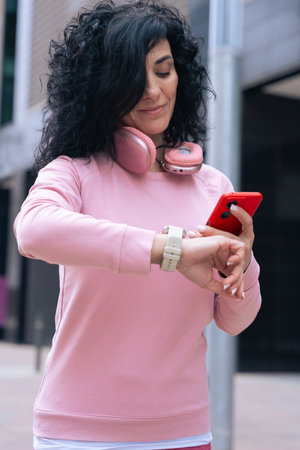 Caucasian woman checking smartwatch outdoors in urban area, wearing pink sweatshirt.の写真素材