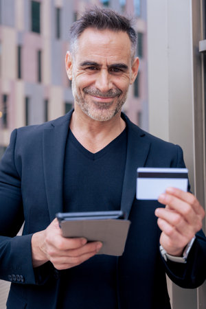 Smiling caucasian man making online payment with credit card and tablet in outdoor settingの写真素材