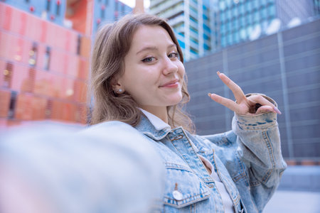 Caucasian student taking selfie and making peace sign in modern urban environmentの写真素材