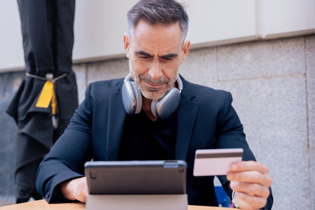 Serious caucasian man making online payment with credit card and tablet in outdoor settingの写真素材