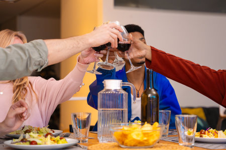 Group of multicultural friends making a toast with red wine glasses during a festive dinner