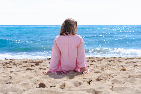 Rear view of woman sitting on beach facing the sea on a peaceful sunny dayの写真素材