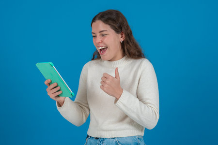 Caucasian woman smiling and giving thumbs up while using tablet on blue background