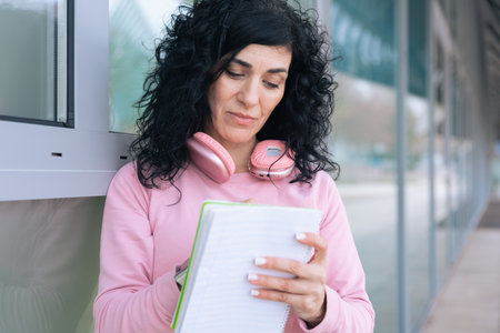 Caucasian female athlete in pink hoodie writing in notebook with headphones on