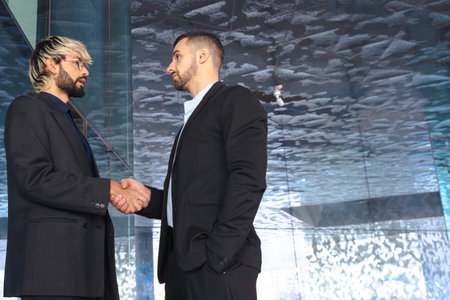 Caucasian businessmen shaking hands in modern glass office environment indoors