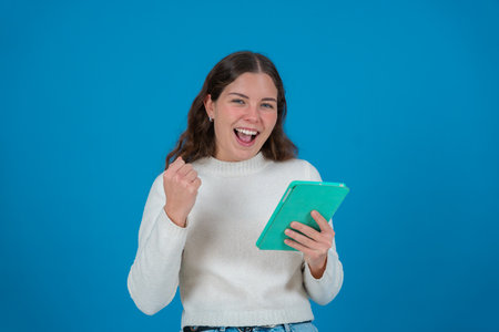 Excited Young Woman Holding Tablet and Celebrating While Looking at the Cameraの写真素材