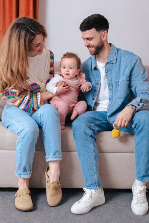 Happy parents playing with baby holding toys while sitting together on sofaの写真素材
