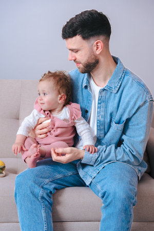 Father holding baby girl on sofa while spending quiet family time at home