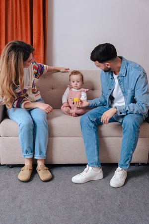 Happy parents playing with baby holding toys while sitting together on sofa