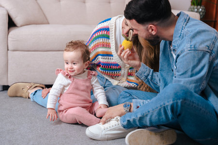 Smiling parents sitting on floor with baby girl holding toy during family moment