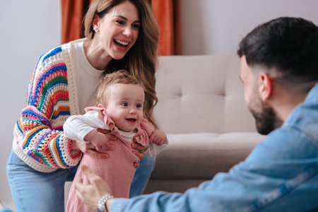 Parents helping baby girl take first steps on carpet at home with joy