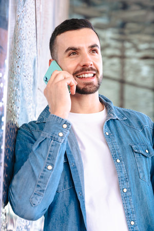 Man talking on smartphone while leaning against glass wall in modern building