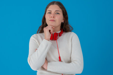 Thoughtful young woman with headphones looking up against blue
