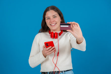 Smiling Woman Showing Credit Card to Camera While Holding Smartphone on Blue Background