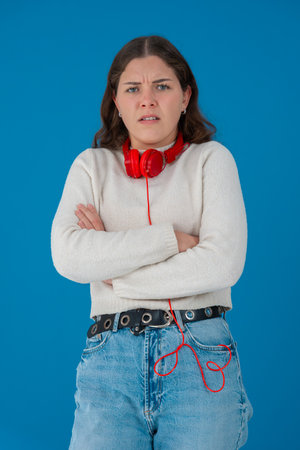 Serious young woman with arms crossed and headphones against blue backgroundの写真素材
