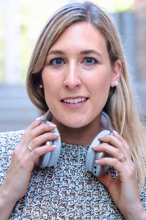 Blonde woman adjusting headphones around neck, smiling at camera, outdoor