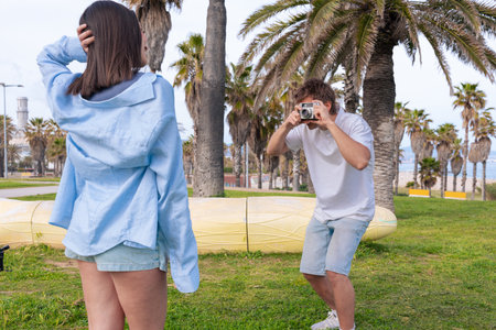 Man photographing young woman posing in a park on a sunny dayの写真素材