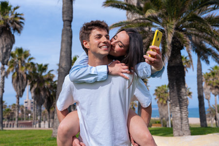 Happy couple taking selfie with smartphone while piggybacking at the beachの写真素材