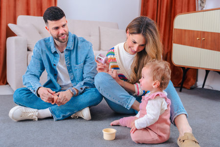 Young parents sitting on floor playing with baby at home family time together