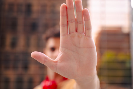 Serious young man with headphones making a stop gesture with his hand outdoorsの写真素材