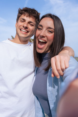 Happy young couple taking cheerful selfie outdoors on sunny day, vertical shot.の写真素材