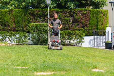 Gardener mowing grass with lawnmower in backyard outdoor maintenance