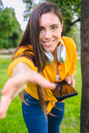 Smiling young woman outdoors reaching hand forward and holding smartphone.の写真素材