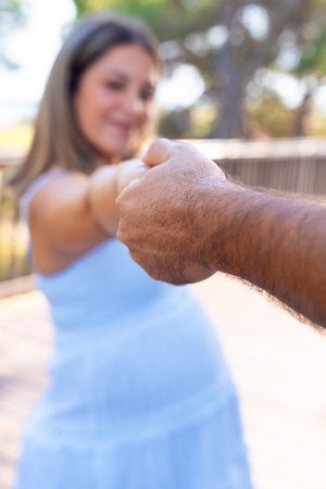 Pregnant woman holding partner hand outdoors on sunny day of love.の写真素材