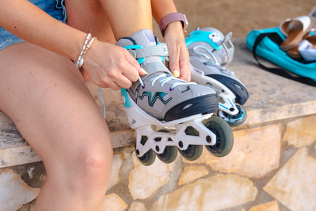 Unrecognizable woman adjusting roller skates sitting outside before skating