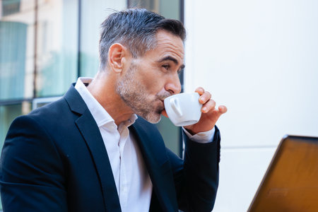Businessman sipping coffee while working on a laptop at an outdoor setting.の写真素材