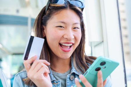Chinese woman holding credit card and smartphone on city tram looking at camera