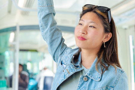 woman smiling while using smartphone and standing inside modern city tramの写真素材