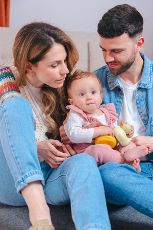 Happy parents playing with baby holding yellow toy at home.Vertical