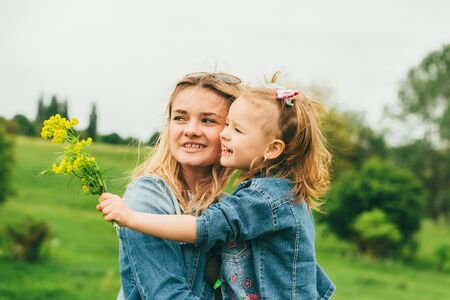 The little girl holds yellow wildflowers in her hand and hugs her mother. The concept is Mothers Day. Mother and daughter in the meadow among the May greenery hug.の写真素材