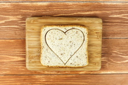 Slice of cereal toast bread with cut out heart shape on wooden cutting board