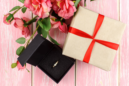 Gift with red ribbon, ring in box and pink flowers. Selective focus.の写真素材