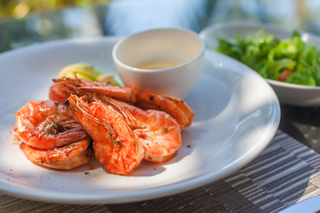 Grilled shrimps on plate with sauce and plate with green salad with tomato. Outdoor photoの写真素材