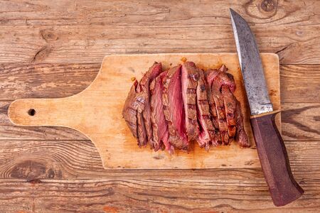 Slices of roast beef meat on wooden cutting board with old knife. Top view.