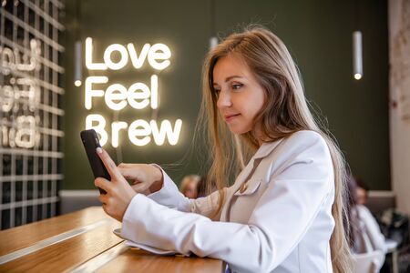 Portrait successful smiling businesswoman sitting in cafeteria using smartphone