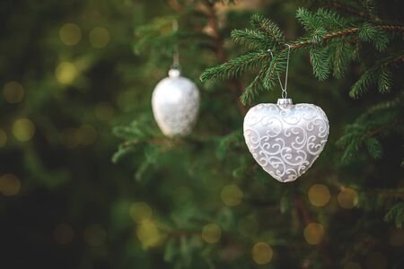 Christmas spruce decoration toys shaped like a heart hanging on a tree branch with bokeh blurred lights. Green wood background. Copy space. Concept of outdoor New Year holiday.の写真素材