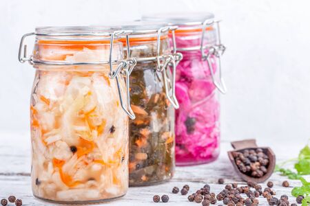 Fermented preserved vegetarian food. Homemade marinated cabbage kimchi, sea kale with carrot, sauerkraut sour in glass jars on rustic wooden kitchen table. Canned vegetables food conceptの写真素材