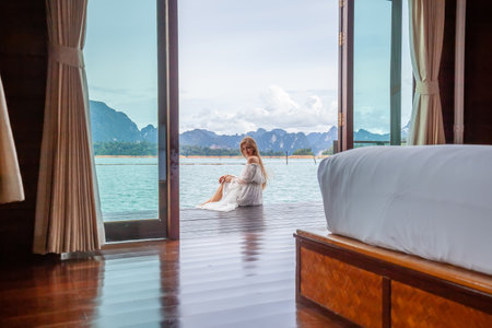 Travel Woman in White Dress Sitting Outdoor near Wooden House on Water