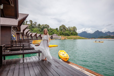 Travel Woman Standing on Pier of Wooden House on Lake with Tropical Mountains
