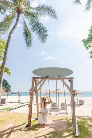 Travel Woman in White Dress and Straw Hat Sitting on Wooden Wings near Blue Seaの写真素材