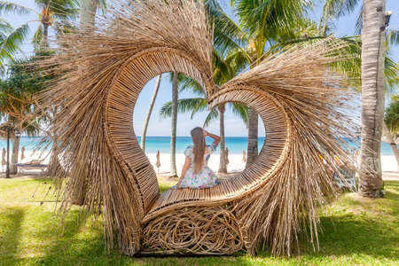 Back View of Tourist Woman Sitting in Photo Spot like Straw Heart with Palm Treeの写真素材