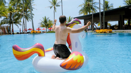 Funny man having fun, dancing on floating inflatable unicorn, tropical vacation