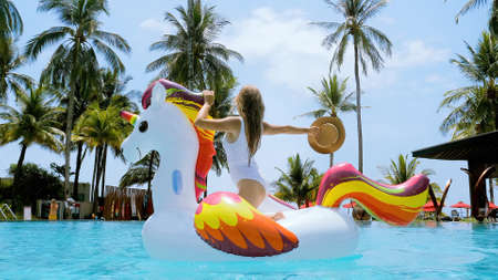 Vacation woman on inflatable unicorn float mattress having fun in swimming pool