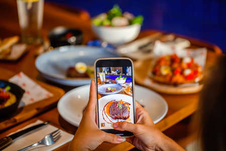 Woman photographing gourmet steak on mobile phone at luxury restaurant table